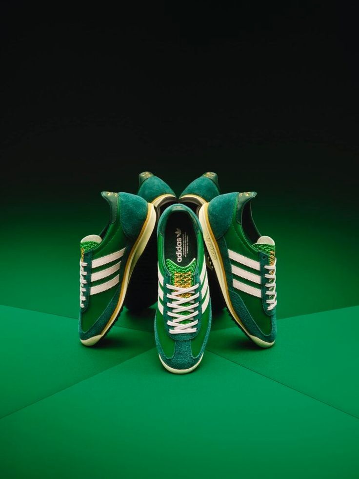 Green Adidas sneakers with white stripes displayed on a green background.